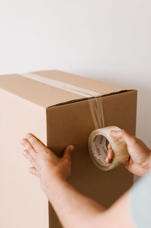 Worker sealing a cardboard box with acrylic packing tape